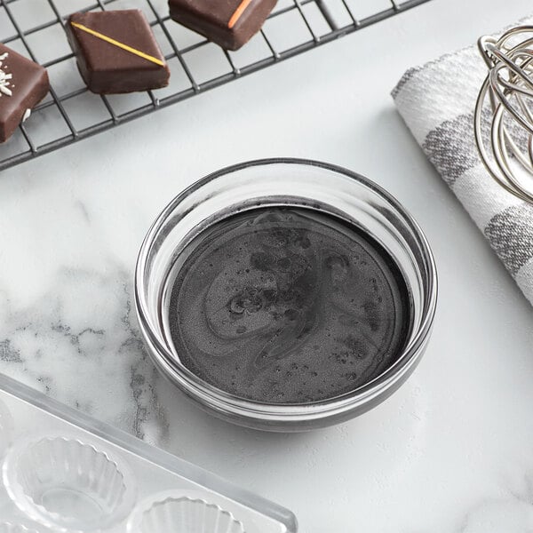 A bowl of black liquid next to chocolates on a wire rack.