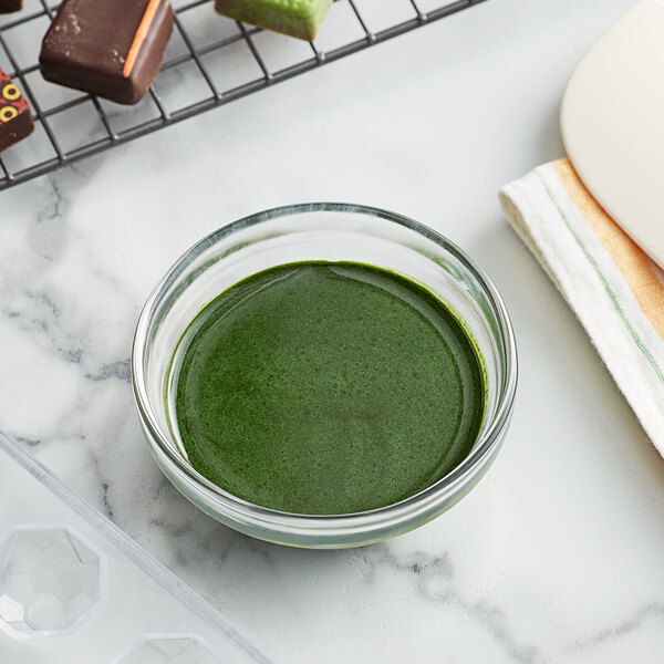 A bowl of green liquid next to a tray of chocolates.