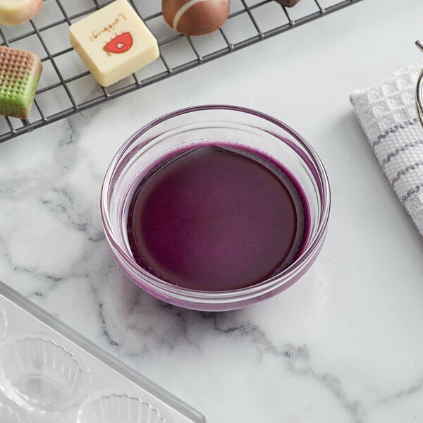 A bowl of purple liquid next to a tray of chocolates.