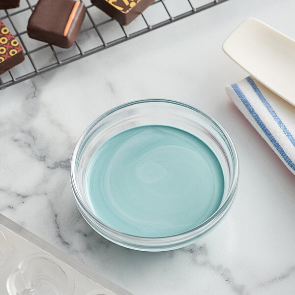 A bowl of blue cocoa butter next to chocolates on a kitchen counter.