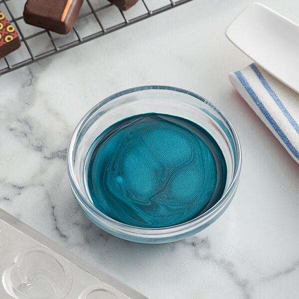 A bowl of blue liquid next to a tray of chocolates.