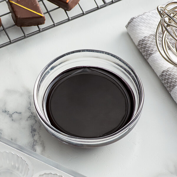 A bowl of liquid chocolate next to a pan of chocolate.