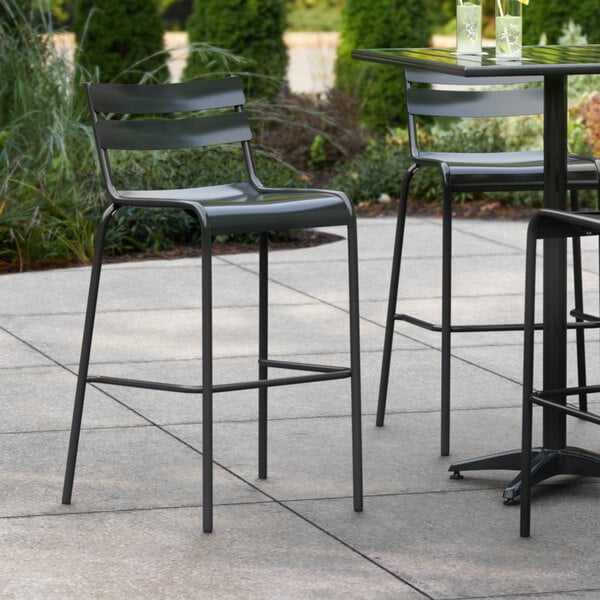 A set of four Lancaster Table & Seating black bar stools on a patio.