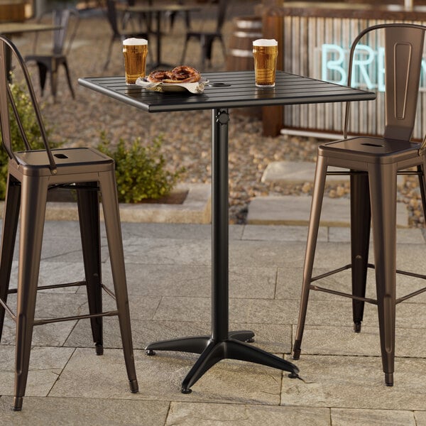 A black powder-coated aluminum bar height outdoor table with a square top and umbrella hole, shown with two metal bar stools.
