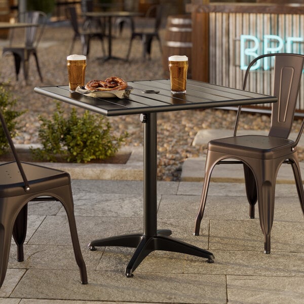 A black powder-coated aluminum outdoor dining table with an umbrella hole, shown with drinks and snacks on top.