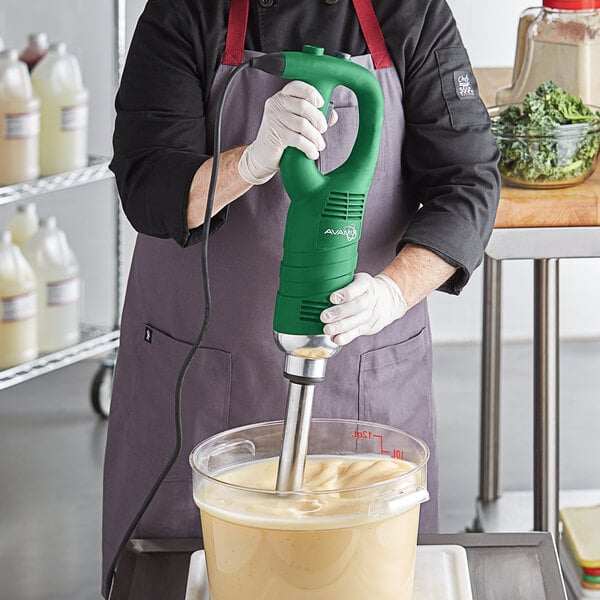 A person using an AvaMix medium-duty immersion blender to mix green food in a bowl.