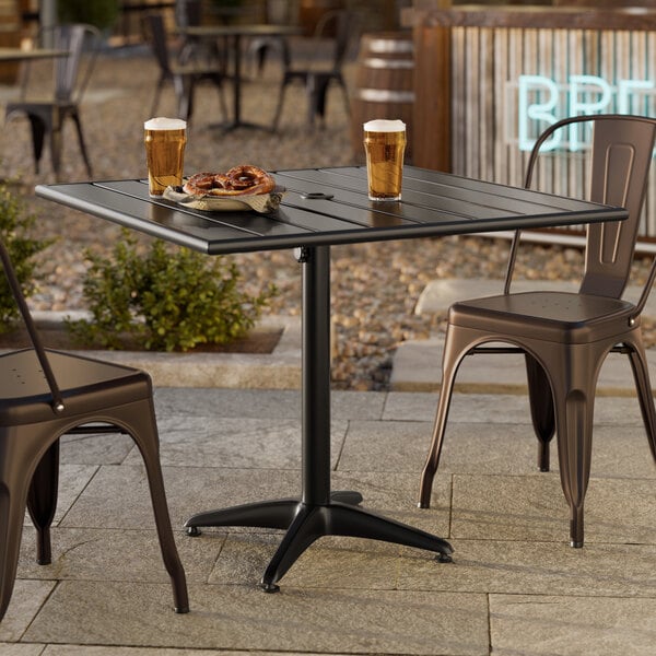 A square black powder-coated aluminum outdoor dining table with an umbrella hole, shown with two metal chairs.