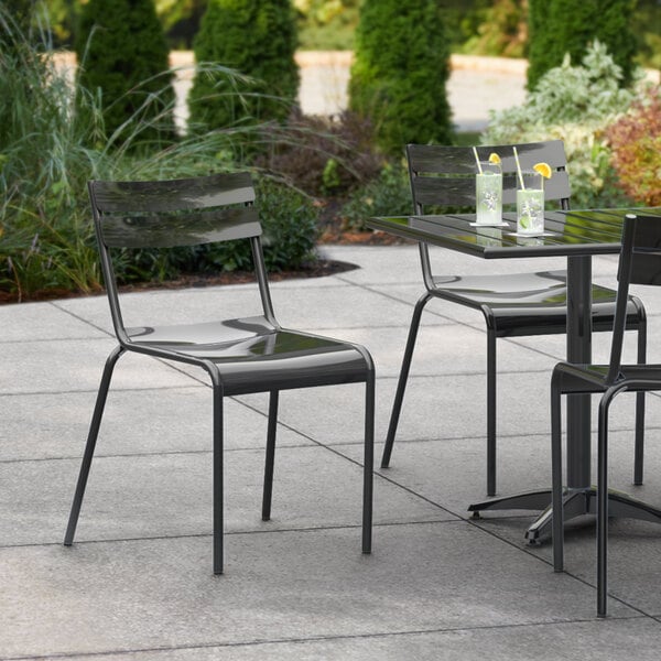 A Lancaster Table & Seating black powder coated aluminum outdoor side chair on a patio with drinks on the table.