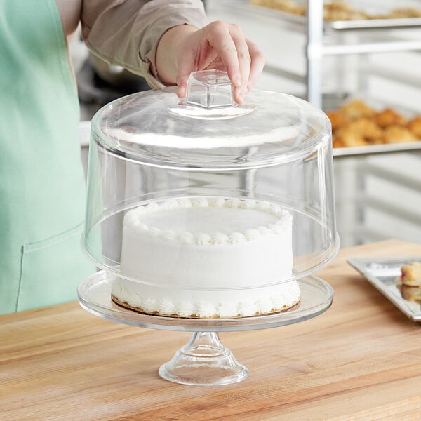 A person holding a cake covered with an American Metalcraft clear plastic cake cover.