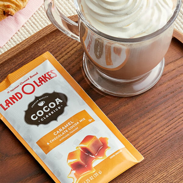 A glass of Land O Lakes Caramel and Chocolate hot cocoa next to a packet of confectionery.