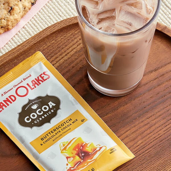 A glass of chocolate milk next to a packet of Land O Lakes Cocoa Classics Butterscotch and Chocolate.