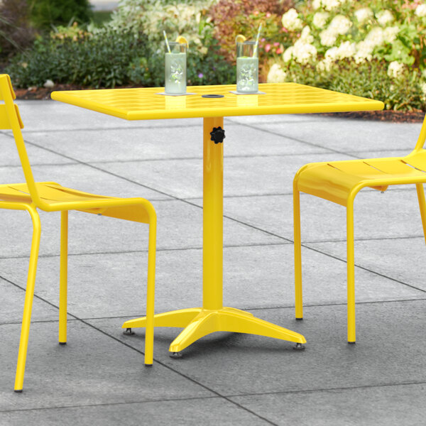 A yellow Lancaster Table & Seating dining height table with two chairs on an outdoor patio.