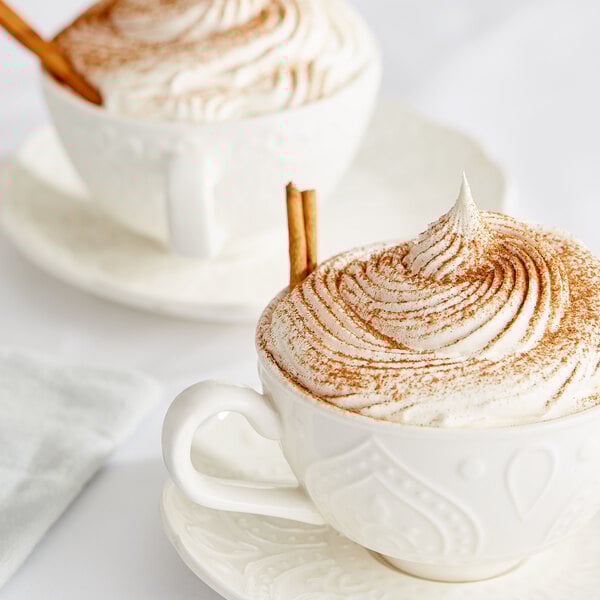 A white cup of coffee with brown and white whipped cream and ground Ceylon cinnamon.