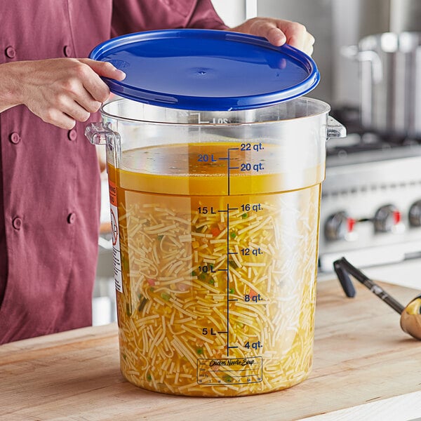 A person holding a blue lid over a large clear food storage container.