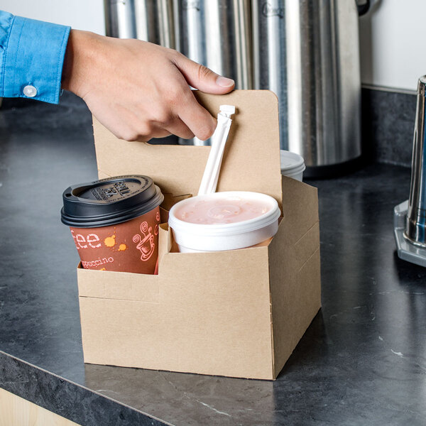 A hand using a Sabert tall drink carrier to hold four brown cups with black lids.