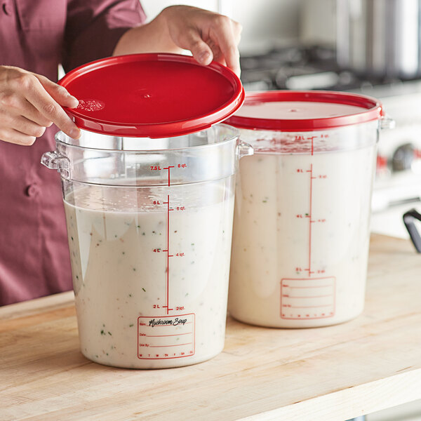 A woman pouring white liquid into a Vigor clear polycarbonate food storage container with a red lid.