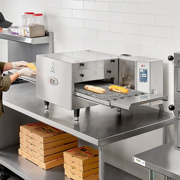 A woman in a professional kitchen using a Cooking Performance Group countertop conveyor oven.
