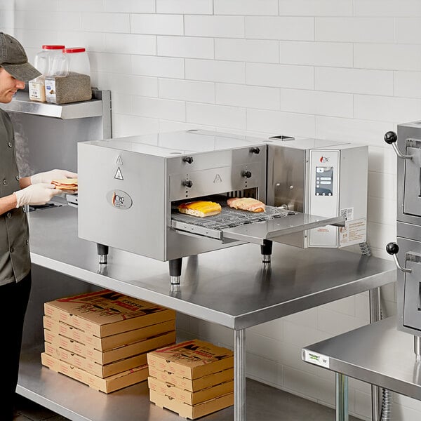 A man in a professional kitchen wearing gloves putting food into a Cooking Performance Group conveyor oven.