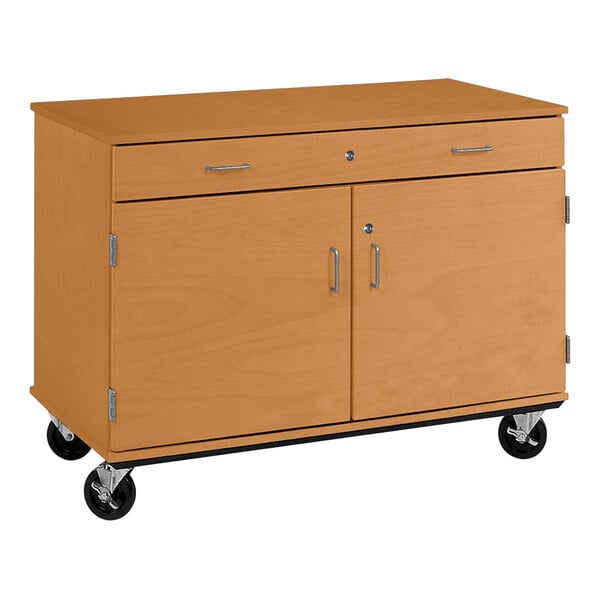A light oak I.D. Systems wooden cabinet on wheels with two doors and a drawer.