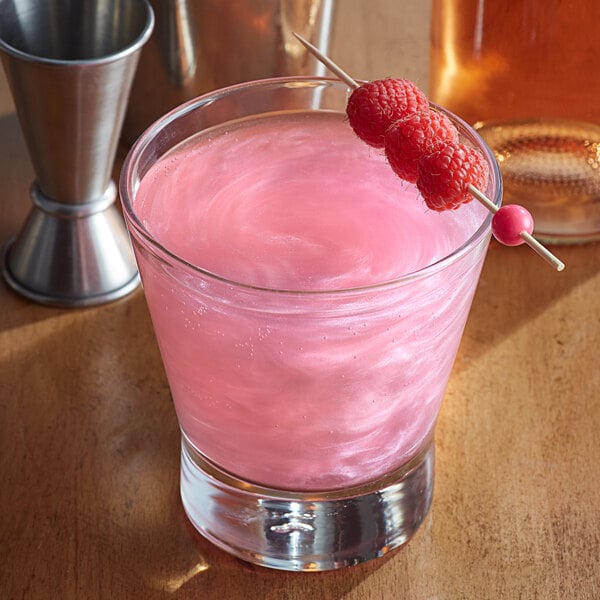 A glass of pink drink with Spirdust Pink Cocktail Shimmer and raspberries on a toothpick.
