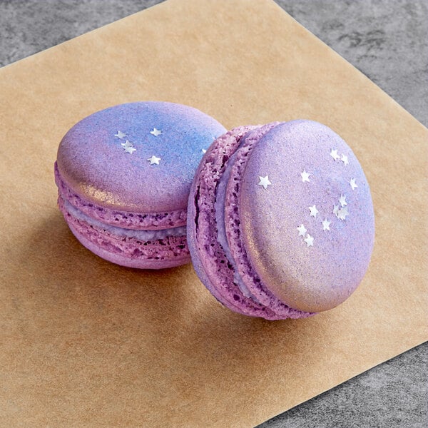 Two purple and white Macaron Centrale Neptune macarons on a brown surface.