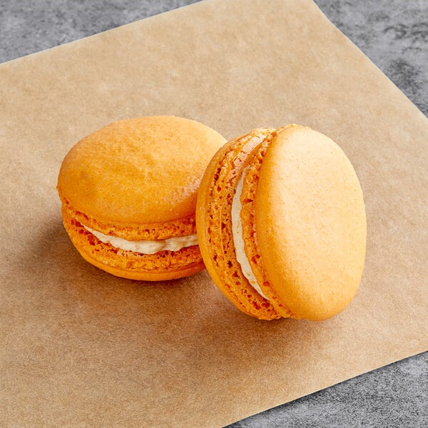 Two pumpkin buttercream macarons on a brown paper.