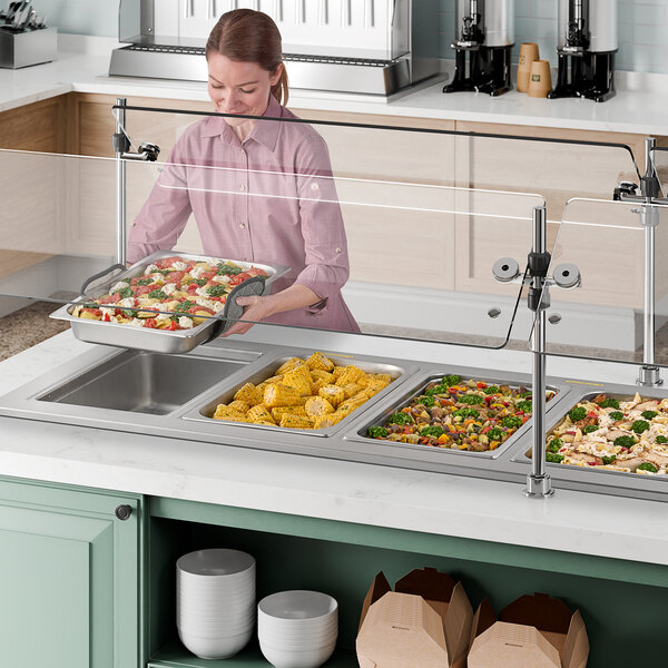 A woman using a Delfield drop-in hot food well to serve food on a tray.