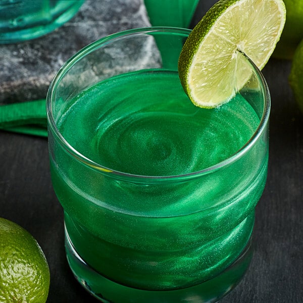 A glass of green cocktail with a lime wedge on the rim.