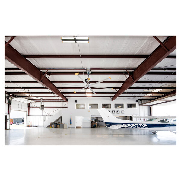 A Big Ass Fans yellow and silver aluminum ceiling fan hanging in a shop with an airplane inside.