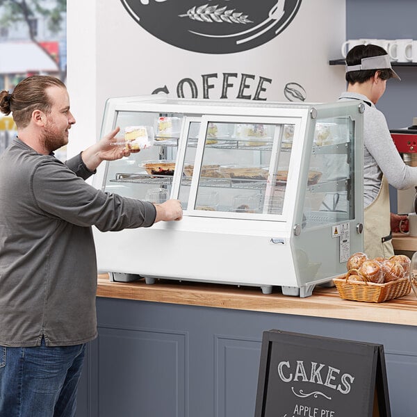 A man standing in front of a white Avantco self-serve bakery display case.
