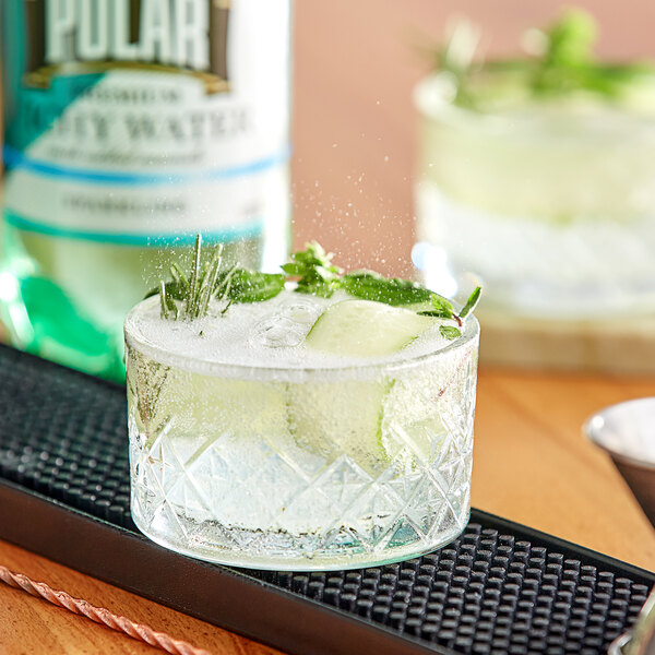 A glass of ice water with cucumber slices on a table.