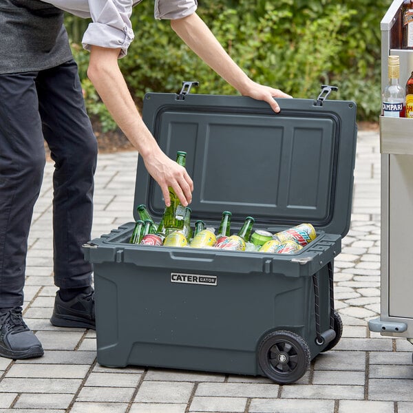 A man using a CaterGator charcoal outdoor cooler to chill bottles on a cart.