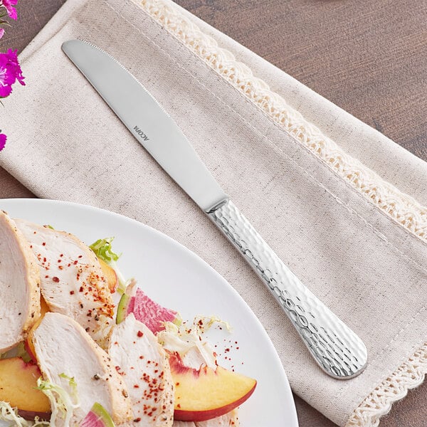 An Acopa Inspira stainless steel dinner knife next to a plate of food with a piece of meat.