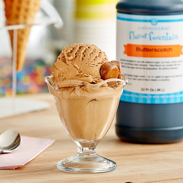 A bowl of ice cream with a scoop and LorAnn Butterscotch syrup in a glass on a counter.