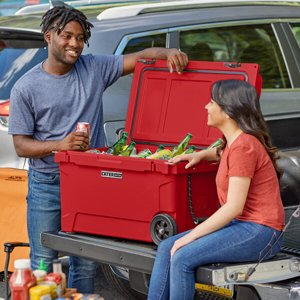 A man and woman sitting on the back of a truck next to a red CaterGator cooler.