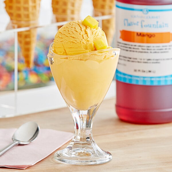 A glass with a scoop of yellow ice cream and a bottle of LorAnn Mango Flavor Fountain syrup on a table.