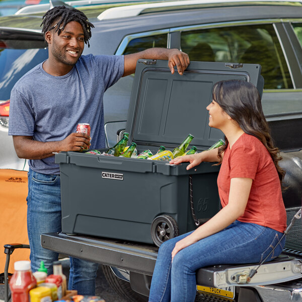 A man and woman sitting on the back of a truck with a CaterGator cooler.