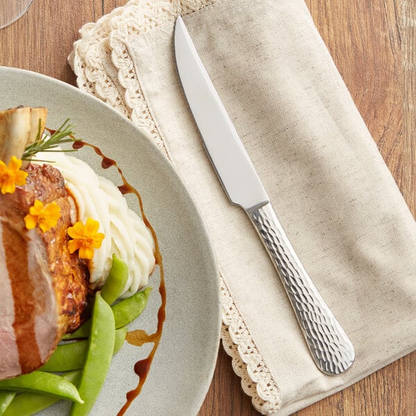 A plate of food with a Acopa Inspira steak knife on a table with a napkin.