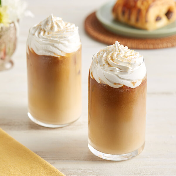 Two glasses of Crown Beverages coffee with whipped cream and a pastry on a white background.