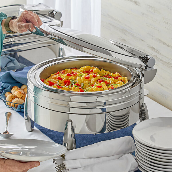 A woman using an Acopa Manchester chafer to serve food from a buffet table.
