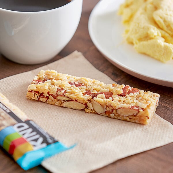 A KIND Almond & Coconut bar on a napkin next to a plate of food.