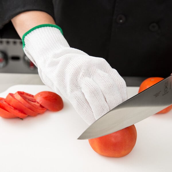 A person wearing a Victorinox cut resistant glove cutting a tomato.