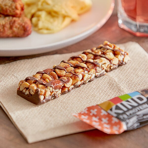 A KIND Peanut Butter Dark Chocolate bar on a napkin next to a package of more bars.