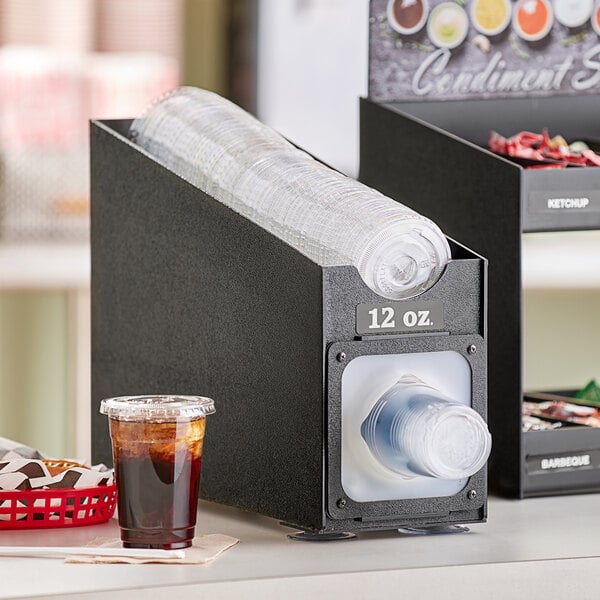 A black KleanTake countertop cup dispenser with a white lid on top holding plastic cups.