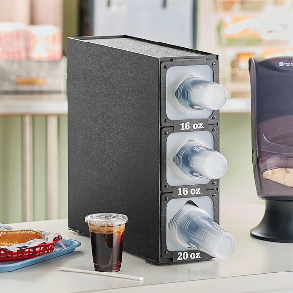 A black KleanTake countertop cup dispenser with plastic cups inside.