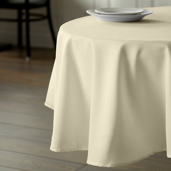 An ivory table with a white Intedge round tablecloth and a white plate on it.