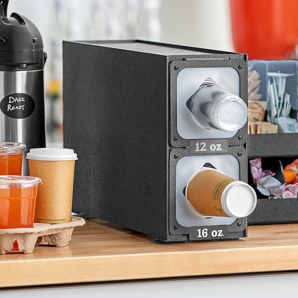 A black KleanTake countertop cup dispenser with two cups in it.