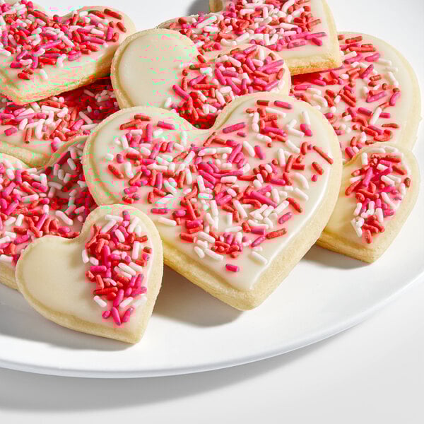 A plate of heart-shaped sugar cookies decorated with white icing and red, pink, and white sprinkles.