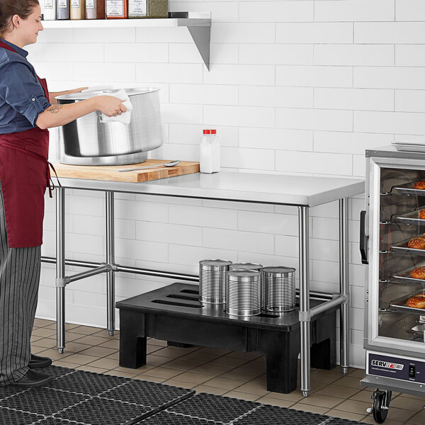 A woman in a red apron using a large stainless steel table.