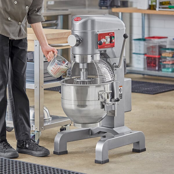 A person in black pants pouring milk into an Avantco floor mixer.